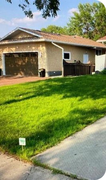 A thick green lawn along a driveway in front of a stucco house